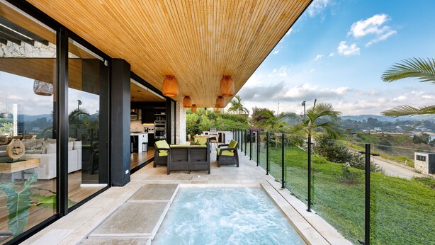 A modern outdoor pool area with a wooden ceiling, glass walls, and a view of the landscape.