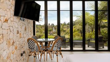 A room with a stone wall, a flat-screen TV, a round table with chairs, and a bed.