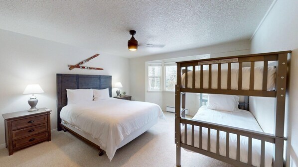A bedroom with a large bed, two bedside tables with lamps, a wooden headboard, a bunk bed, and a ceiling light fixture.