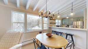Un comedor con una mesa y sillas de madera, una araña y vistas a un paisaje nevado a través de amplios ventanales.