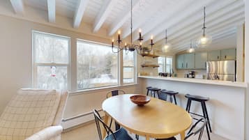 A dining area with a wooden table and chairs, a chandelier, and a view of a snowy landscape through large windows.