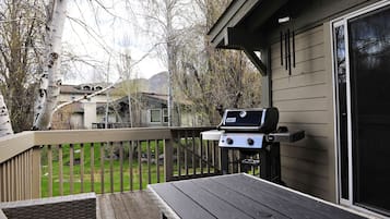 A deck with a grill, a table, and a view of a backyard with trees and houses.