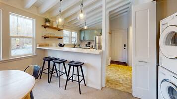 A modern kitchen with a bar area, a dining table, and a washing machine.