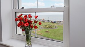 A window with a clear view of a parking area and a grassy landscape. - Sandsend View (Whitby)