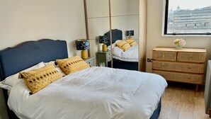 Ein Schlafzimmer mit einem Bett, einem Schminktisch, einem Spiegel und einem Fenster mit Blick auf Gebäude.