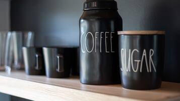 Una fila di contenitori neri con le scritte 'COFFEE' e 'SUGAR', posti su un ripiano di legno.
