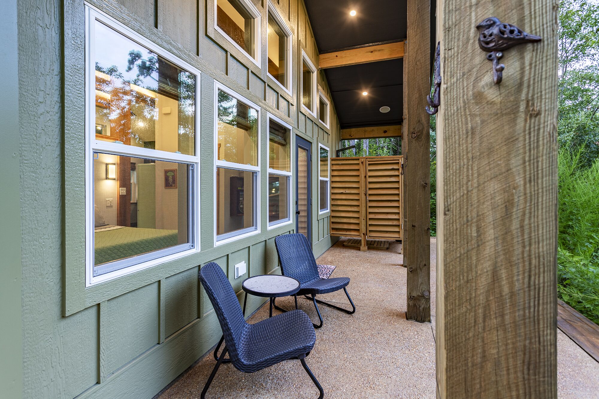 A covered patio with two wicker chairs and a small table, large windows, and a wooden door with a bird-shaped handle.