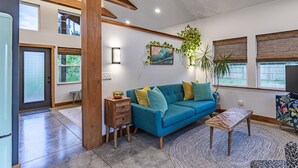 A modern living room with a teal sofa, wooden accents, a small side table, and a patterned rug. - Kitty Hawk Reserve OBX Tiny House! Hot Tub & Beach included! (Kitty Hawk)