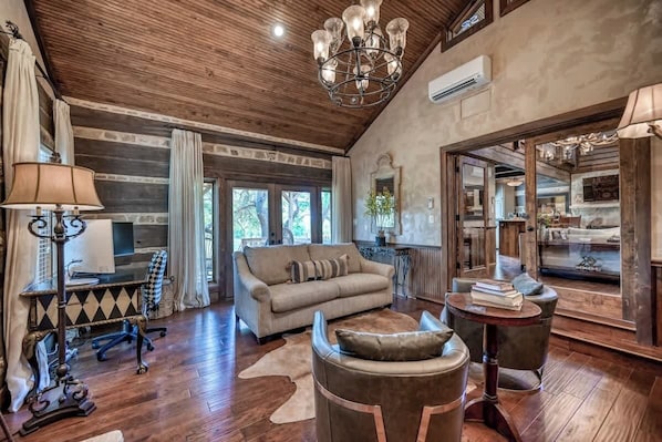 A spacious living room with a wooden ceiling, a beige sofa, a leather armchair, and a small round table.