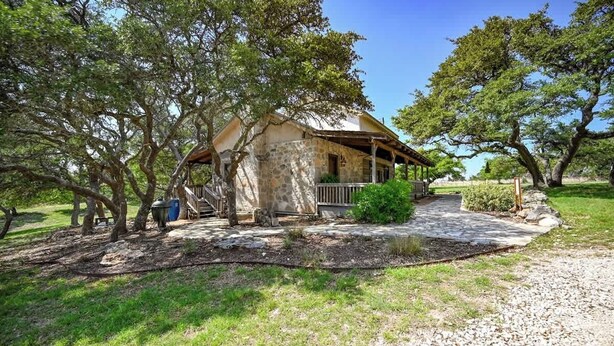 Une maison en pierre avec un porche en bois, entourée d’arbres et bordée d’une allée gravillonnée.