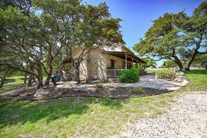 A stone house with a wooden porch, surrounded by trees and a gravel driveway. - Luxury 23-ac Ranch Casita w/Hot tub! (Fredericksburg)