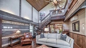 Un vaste salon doté d’un haut plafond, d’un escalier en bois et d’un lustre.