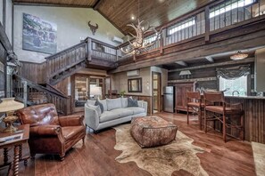 A spacious living area with a high ceiling, a staircase, a chandelier, and rustic decor.
