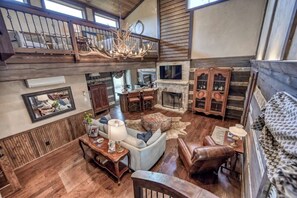 A spacious loft-style living area with a high ceiling, wooden floors, a fireplace, and a television mounted above it. - Luxury 23-ac Ranch Casita w/Hot tub! (Fredericksburg)