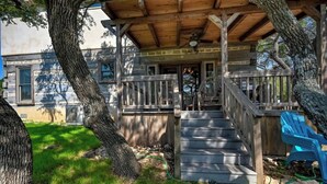 A wooden deck with a staircase leading to a covered porch, surrounded by trees and a grassy yard.