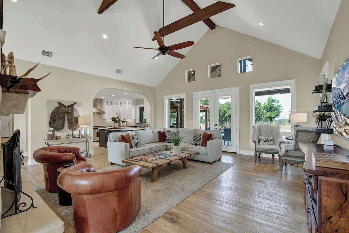 A spacious living room with a high ceiling, a wooden coffee table, leather sofas, and a large TV.