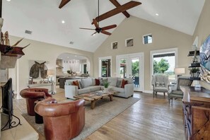 A spacious living room with a high ceiling, a wooden coffee table, leather sofas, and a large TV. - Lux Ranch w/Pool-Hot-Tub Near Fred! (Fredericksburg)