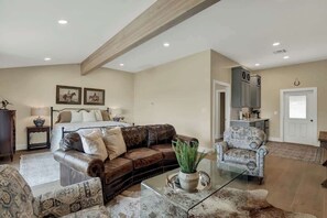 Ein geräumiges Wohnzimmer mit einer Ledersofa, einem gemusterten Sessel und einem Glastisch.