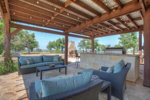 An outdoor patio with wicker furniture, a stone barbecue area, and a view of the surrounding landscape. - Lux Ranch w/Pool-Hot-Tub Near Fred! (Fredericksburg)