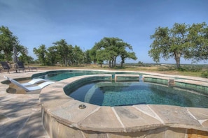 A swimming pool with a curved design, surrounded by stone tiles and shaded by trees. - Lux Ranch w/Pool-Hot-Tub Near Fred! (Fredericksburg)