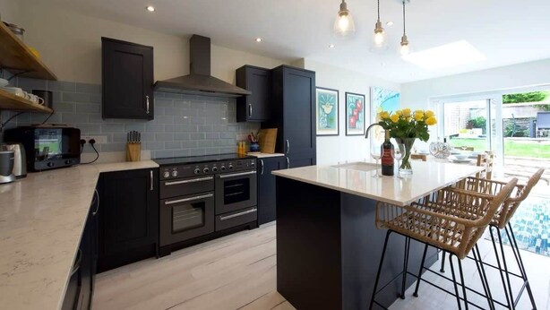 Una cocina moderna con armarios oscuros, una isla central e iluminación colgante.