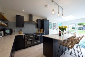 Une cuisine moderne avec des meubles de couleur sombre, un îlot central et des luminaires suspendus.