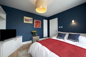 Une chambre à coucher avec un lit, un téléviseur posé sur un meuble, une porte et un mur orné de deux tableaux encadrés.