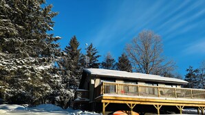 A wooden cabin with a balcony, surrounded by snow-covered trees and a clear blue sky. - Cozy lakeside cottage with breathtaking views & amazing fishing  (Yarker)