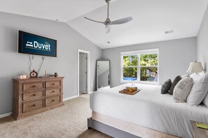 Relax in this serene bedroom with a large bed positioned against a window, a flat-screen TV, and a wooden dresser.