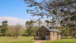 A stone cottage with a small porch, a table with chairs, and a fenced pasture in the background. - Herdie Hideaway (Appleby-in-Westmorland)