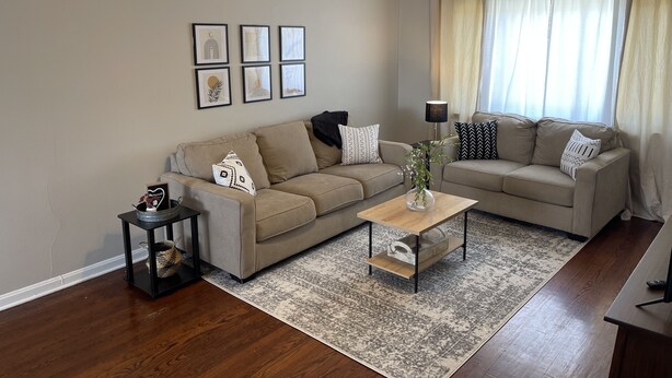 Ein Wohnzimmer mit zwei beigen Sofas, einem Couchtisch, gerahmten Bildern an der Wand und einem Deckenventilator.