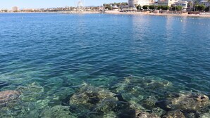 A coastal area with clear water, rocks, and buildings including a Ferris wheel in the background. - Beautiful new 2-room apartment, Saint-Raphael golf course, close to beaches (Saint-raphael)