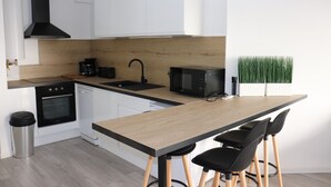 A modern kitchen with white cabinets, a wooden countertop, a black range hood, a coffee maker, a microwave, and a bar stool. - Beautiful new 2-room apartment, Saint-Raphael golf course, close to beaches (Saint-raphael)