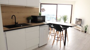 A modern kitchen with a black microwave, a sink, and a wooden backsplash. There are two black chairs and a small table. - Beautiful new 2-room apartment, Saint-Raphael golf course, close to beaches (Saint-raphael)