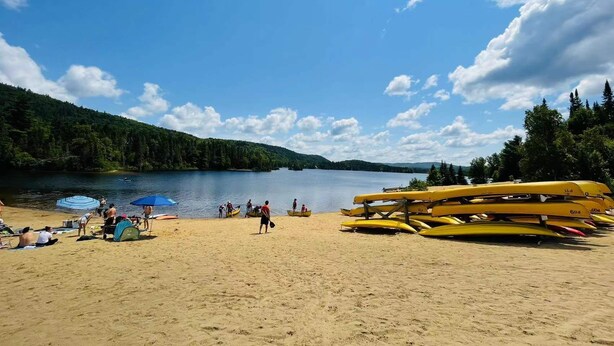 Una playa con kayaks y canoas, una tienda de campaña y gente cerca del agua.