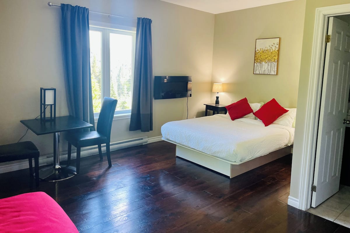 A hotel room with a bed, a desk, a chair, a TV, a lamp, and a window with curtains.