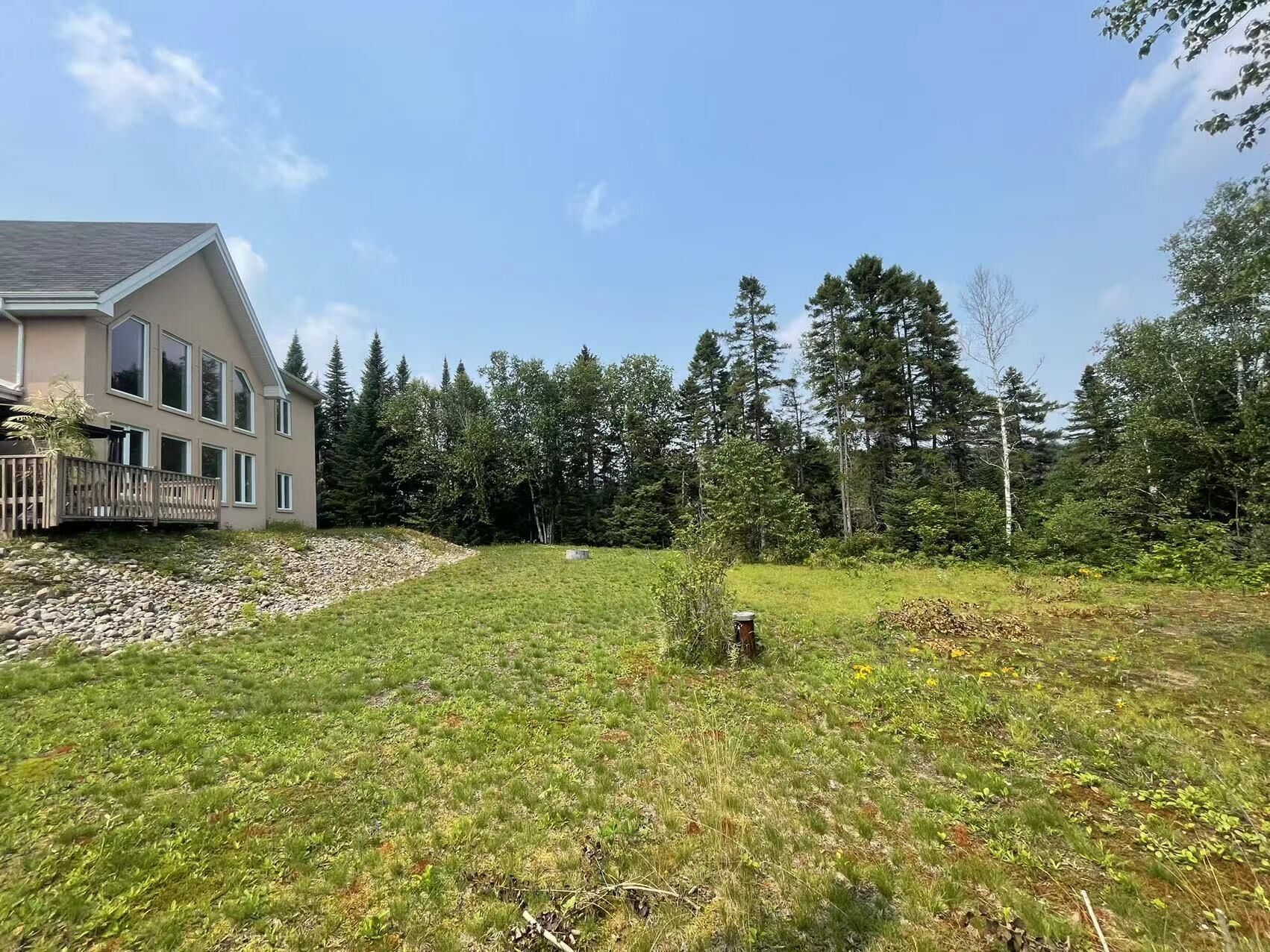 A house with a large deck, surrounded by a grassy yard and dense forest.