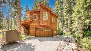 Eine zweistöckige Blockhütte mit Garage, umgeben von einem Wald.