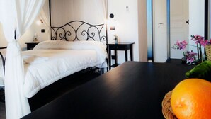 A bedroom with a four-poster bed, a bedside table with a lamp, and a small table with a vase of flowers. - Hotel Residence Noto Marina e Spa (Noto)