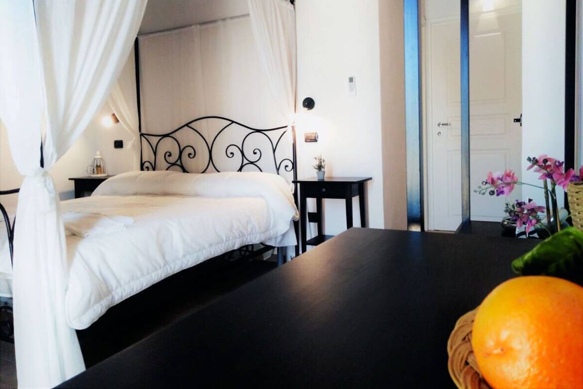A bedroom with a four-poster bed, a bedside table with a lamp, and a small table with a vase of flowers.