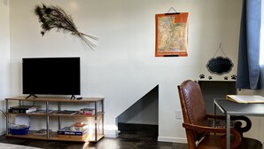 A living room with a TV on a wooden stand, a map on the wall, and a chair with a leather backrest.