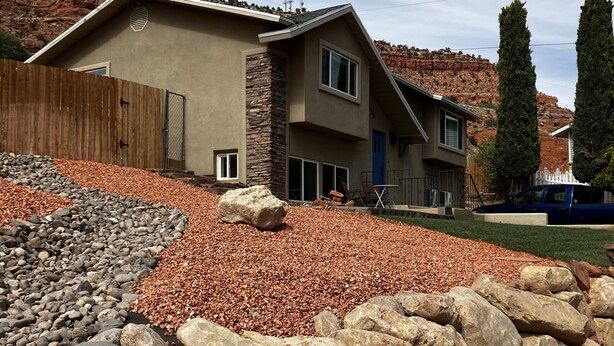 A modern two-story house with a stone facade, large windows, and a well-maintained front yard with rocks and gravel.