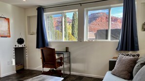A room with a desk, chair, and a couch. There is a window with a view of mountains.