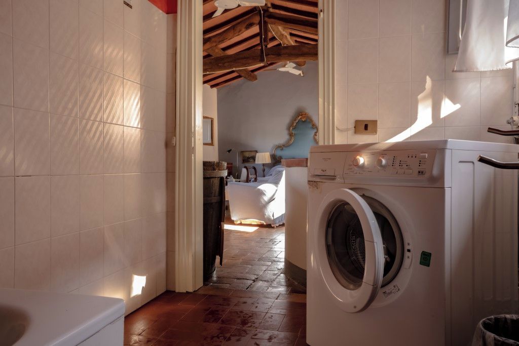 A laundry room with a washing machine, a tiled wall, and a wooden floor.