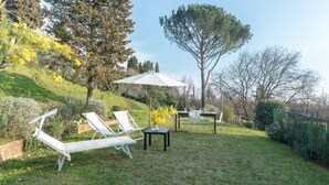 Een gazon met een buitenzitplaats, twee lounge fauteuils, een tafel en een parasol.