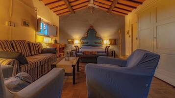 A cozy room with a bed, a sofa, and two armchairs. There is a wooden ceiling and a white door in the background.