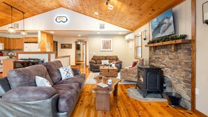 A spacious living area with a stone fireplace, wooden ceiling, and a cozy seating arrangement.