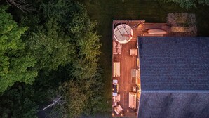 An aerial view of a wooden deck with a dining table and chairs, surrounded by dense foliage.