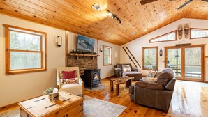 A cozy living room with a fireplace, wooden floors, and large windows.