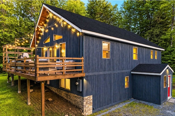 Une maison moderne en bois, dotée d’une terrasse, de nombreuses fenêtres et d’un petit abri attenant.